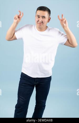 Fröhlicher junger Kerl, der Siegeszeichen zeigt und im Studio glücklich aussieht Stockfoto