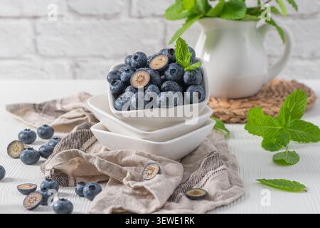 Ein Stapel weißer Keramikschalen gefüllt mit frischen, tau bedeckten Heidelbeeren, garniert mit lebendiger Minze, auf einem rustikalen Leinentuch gegen einen Hauch gelegt Stockfoto
