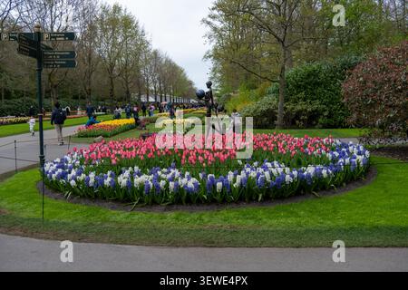 Fußgängerszene in den Gärten Keukenhof mit Wegweisern, Frühlingsblumenbeeten, Besuchern und Gartenskulpturen in Lisse, Niederlande. Stockfoto