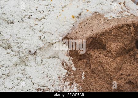 Eine Nahaufnahme eines Hügels aus feinem weißem Chemiepulver oder weißem Sand, der direkt neben einem Haufen von grobem braunem Bausand sitzt. Stockfoto