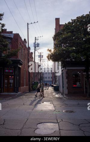 Silhouetten von Menschen, die bei Sonnenuntergang durch eine schmale historische Gasse mit Gegenlicht gehen. Stockfoto