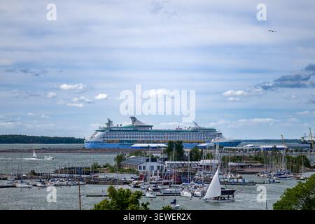Großes Luxus-Kreuzfahrtschiff, das an einem geschäftigen Hafen liegt, der mit Segelbooten und Yachten gefüllt ist, an einem klaren Tag. Stockfoto