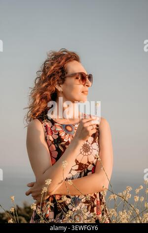 Frau blüht Sonnenuntergang, stilvolle Frau, die kleine Wildblume im Feld während Sonnenuntergang mit Kopierraum für Textplatzierung hält Stockfoto