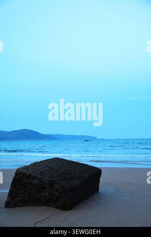 Betonbruchstein am Sandstrand mit Hintergrund der Bergküste Stockfoto