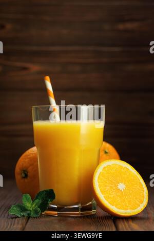 Glas frisch gepresster Orangensaft mit gestreiftem Strohhalm, Minze und Zitrusfrüchten auf rustikalem Holzuntergrund Stockfoto