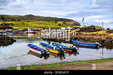 Kleine farbenfrohe Fischerboote legen im friedlichen Hafen von Hanga Piko an, mit der Statue Ahu Riata Moai im Hintergrund auf der Osterinsel, Chile. Stockfoto