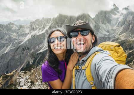 Fröhlich glückliche zwei Wanderfreunde, die Selfie am Aussichtspunkt Cadini di Misurina machen. Millennial Guy Girl genießt Sommerausflüge und lacht Stockfoto