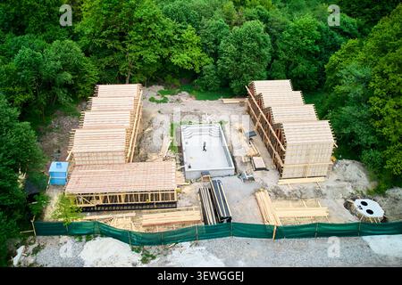 Aus der Vogelperspektive der Baustelle mit Holzunterkünften und zentralem Pool, wo ein Mann im Becken steht und Architekt oder Arbeiter repräsentiert, der den Fortschritt und die Grundrisse der Baustelle überprüft Stockfoto