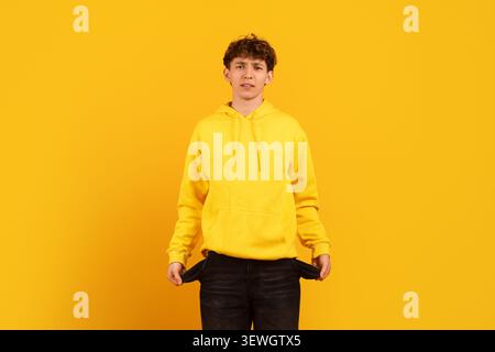 Besorgter junger Kerl im Hoodie mit leeren Taschen auf gelbem Studiohintergrund Stockfoto