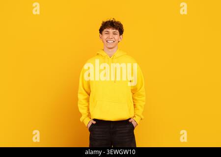 Junger Mann im Kapuzenpullover, der mit Händen in Taschen auf gelbem Hintergrund steht Stockfoto