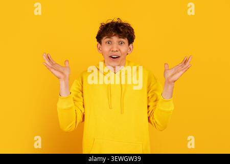 Überraschter Kerl in gelbem Hoodie, der mit offenen Händen auf gelbem Hintergrund zuckt Stockfoto