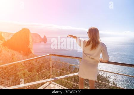Frau Meer Balkon Frau zeigt in Richtung des blauen Ozeans von einem malerischen Küstenaussichtspunkt an einem hellen sonnigen Tag Stockfoto
