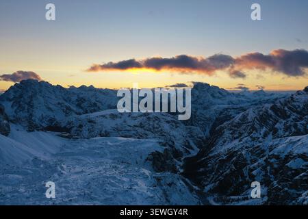 Aus der Vogelperspektive auf die schneebedeckten Gipfel der Tre Cime di Lavaredo bei Sonnenaufgang mit goldenem Licht, das die Wolken über den zerklüfteten Dolomiten in Auron trifft Stockfoto