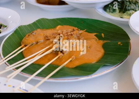 Indonesischer Satay mit Erdnusssauce serviert auf Bananenblatt-Teller Stockfoto