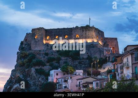 Beleuchtete Burg Ruffo auf einer felsigen Klippe in der Abenddämmerung in Scilla, Italien Stockfoto