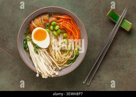 Asiatische Ramen-Nudeln mit Hähnchenscheibe, Enoki-Pilzen, Karotten, Edamame-Bohnen und Ei in einer Schüssel. Draufsicht Stockfoto