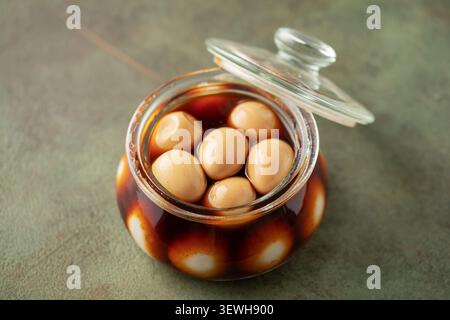 Hausgemachte, braun marinierte, eingelegte Wachteleier im Glas auf dem Tisch. Asiatische Küche Stockfoto