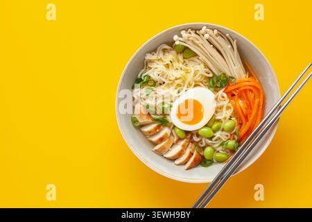 Asiatische Ramen-Nudeln mit Hähnchenscheibe, Enoki-Pilzen, Karotten, Edamame-Bohnen und Ei in einer Schüssel. Draufsicht Stockfoto