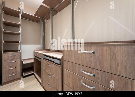 Moderner begehbarer Kleiderschrank mit Holzgarderobensystem, leeren Schubladen, Regalen und Kleiderstangen in einem luxuriösen Ankleidezimmer-Interieur Stockfoto