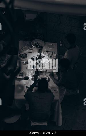 Blick aus einem hohen Winkel auf Freunde, die sich um einen glühenden Tisch versammelten, bei Essen und Wein im Dunkeln, während sie an einem warmen Sommerabend abends ein Essen teilten. Hallo Stockfoto