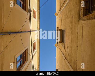 Blick zwischen zwei Gebäuden in Rethymno Kreta mit hellblauem Himmel darüber und einigen Stromleitungen sichtbar Stockfoto