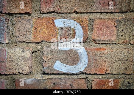Nummer 3 in verblasster weißer Farbe an einer Ziegelwand Stockfoto