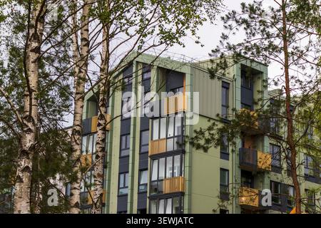 Modernes olivgrünes Apartmentgebäude mit modernen Balkonen, die von Birken und Kiefern eingerahmt sind, in einem umweltfreundlichen Viertel. Stockfoto