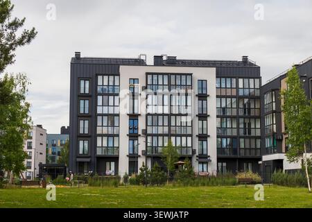 Moderner Wohnblock mit dunkler Metall- und weißer Putzfassade mit Blick auf einen breiten grünen Rasen in der Nachbarschaft. Stockfoto