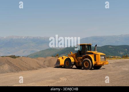 Schwerer industrieller Rollverdichter, der auf einem großen Hügel aus zerquetschtem Stein und Kies unter klarem blauen Himmel auf einem hellen sonnigen d steht Stockfoto