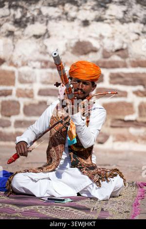 Traditioneller Rajasthani-Volksmusiker in farbenfroher Kleidung, der im Freien ein traditionelles Streichinstrument in Rajasthan, Indien, spielt. Foto aufgenommen am Dezember Stockfoto