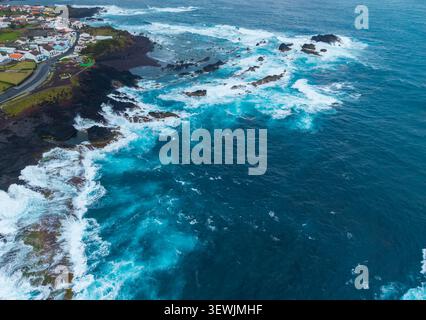 Blick aus der Vogelperspektive auf den Strand von Mosteiros mit stürzenden Wellen gegen vulkanische Felsen und die Küstenstadt Mosteiros, Acores, Portugal. Stockfoto
