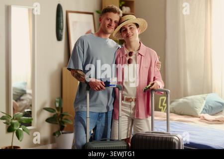 Porträt eines jungen kaukasischen Paares, das mit Koffern posiert, Reisepass und Smartphone hält und sich auf die Urlaubsreise vorbereitet. Ideal für Tourismusmarketing, Reiseplanung und Werbebuchungen Stockfoto