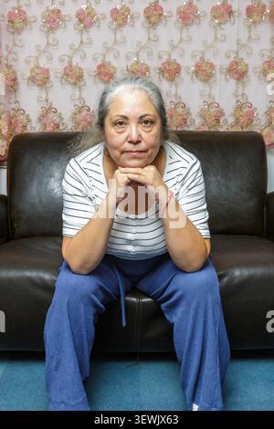 Ältere Frau mit müdem Gesicht und ohne Make-up, ernsthaftem und nachdenklichem Ausdruck, sitzend mit Händen auf dem Kinn und Ellbogen auf den Knien, Pflege der Eiche Stockfoto