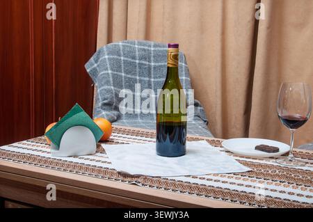 Eine Stillleben-Komposition mit einer Flasche Rotwein, einem Weinglas mit Rotwein, einem kleinen Teller mit Schokolade und Orangen auf einem Tisch mit Dekor Stockfoto