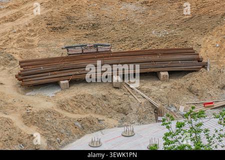 Baustelle mit Bewehrungshaufen, gesichert durch Metallband auf Holzrahmen, rauer Boden mit losem Schmutz, teilweise fertiggestellte Betonplatte im Gitter Stockfoto