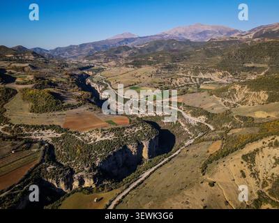 Ein Luftbild fängt den dramatischen Osum Canyon ein, der sich durch eine ländliche Landschaft mit bebauten Feldern und verstreuten Bäumen schlängelt. In der Ferne, robust Stockfoto