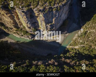 Ein Blick aus der Vogelperspektive fängt den dramatischen Osum Canyon ein, wo sich ein türkisfarbener Fluss durch steile, felsige Klippen windet, die teilweise mit grüner Vegetation bedeckt sind. S Stockfoto