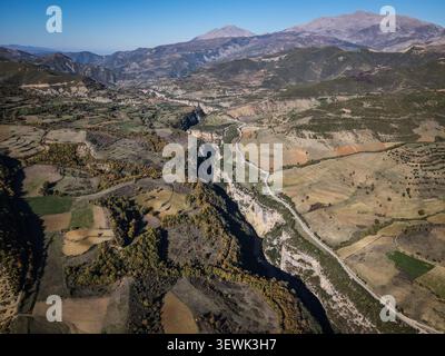 Eine weite Luftaufnahme erfasst den Osum Canyon, der sich durch eine ländliche Landschaft mit Terrassenfeldern, verstreuten Bäumen und einer Straße entlang der schlängelt Stockfoto