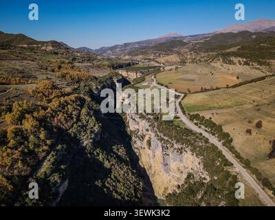 Ein Luftbild fängt den dramatischen Osum Canyon mit steilen Felswänden, einer gewundenen Straße und einem Fluss darunter ein. Die umliegende Landschaft umfasst Ro Stockfoto