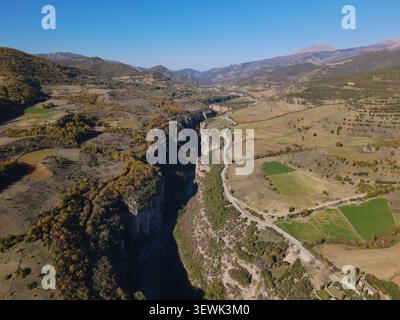 Eine Weitwinkelaufnahme fängt den dramatischen Osum Canyon ein, der sich durch eine ländliche Landschaft schlängelt, flankiert von Feldern und Hängen, die mit Herbstbäumen geschmückt sind. A Stockfoto