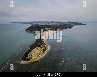 Ein Blick aus der Vogelperspektive fängt die unverwechselbare, zerklüftete Küste des Kap Drastis in Korfu, Griechenland, ein, das sich unter einem bewölkten Himmel bis ins Ionische Meer erstreckt. Das i Stockfoto