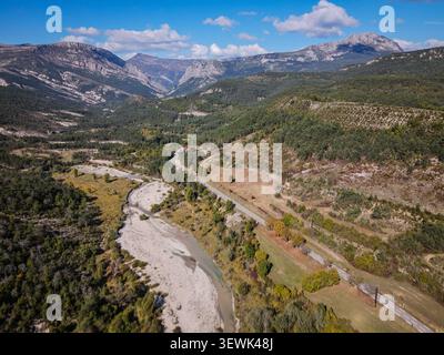 Ein Luftschuss fängt ein gewundenes Flussbett mit flachem Wasser ein, das durch ein Tal fließt, flankiert von einer asphaltierten Straße. Die Landschaft ist grün und Stockfoto