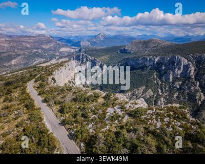 Eine Rundfahrt aus der Vogelperspektive zeigt eine gewundene Asphaltstraße, die durch zerklüftetes, felsiges Gelände mit dünner Vegetation führt. Im Hintergrund, majestätisch Stockfoto