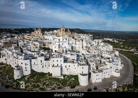 Ein weites Luftbild fängt die historische „Weiße Stadt“ Ostuni, Italien, mit ihrer dichten Ansammlung weiß getünchter Gebäude und der prominenten Kathedrale d ein Stockfoto