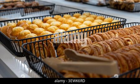 Nahaufnahme von frisch gebackenem Gebäck in Bäckereiblechen, mit Blätterteig, süßen Brötchen und goldenen Backwaren an einem Ladentisch. Stockfoto