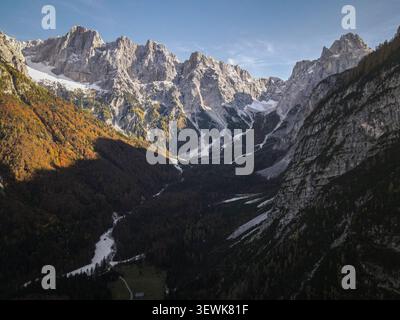 Ein Weitwinkelblick aus der Vogelperspektive fängt die Julischen Alpen ein, mit teilweise verschneiten Gipfeln und einem Tal mit herbstfarbenem Wald Stockfoto
