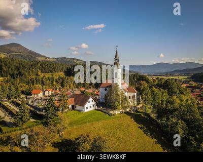 Aus der Vogelperspektive sehen Sie die Sveti Jurij Kirche mit ihrem weißen Glockenturm und dem roten Dach in einem Dorf, umgeben von grünen Feldern und dichten Wäldern. Stockfoto