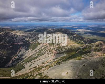 Ein Weitwinkelblick aus der Luft zeigt Gipfel und Täler der Sierra de Guadarrama mit einer gewundenen Schotterstraße und weit entfernten Ebenen in Spanien. Diese ima Stockfoto