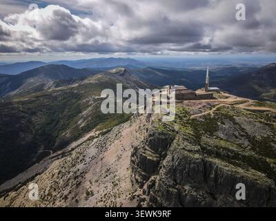 Ein Luftbild erfasst einen Kommunikationsturm und mehrere Gebäude auf einem zerklüfteten Berggipfel am Navacerrada Pass. Umliegende Berge und Stockfoto