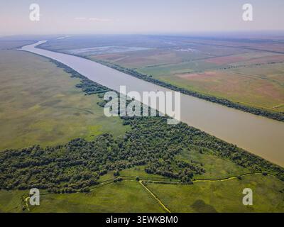 Ein breiter, gewundener Fluss fließt durch ausgedehnte grüne Sumpfgebiete und Felder unter klarem Himmel im Donaudelta in der Ukraine. Diese perspektive Luft Stockfoto